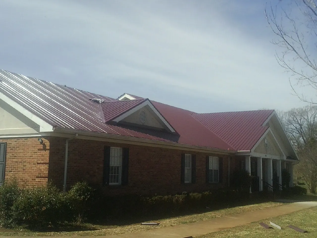 Red metal roof with gabled entries on a long brick building, from a Hail Damage Roof Repair job in Abington