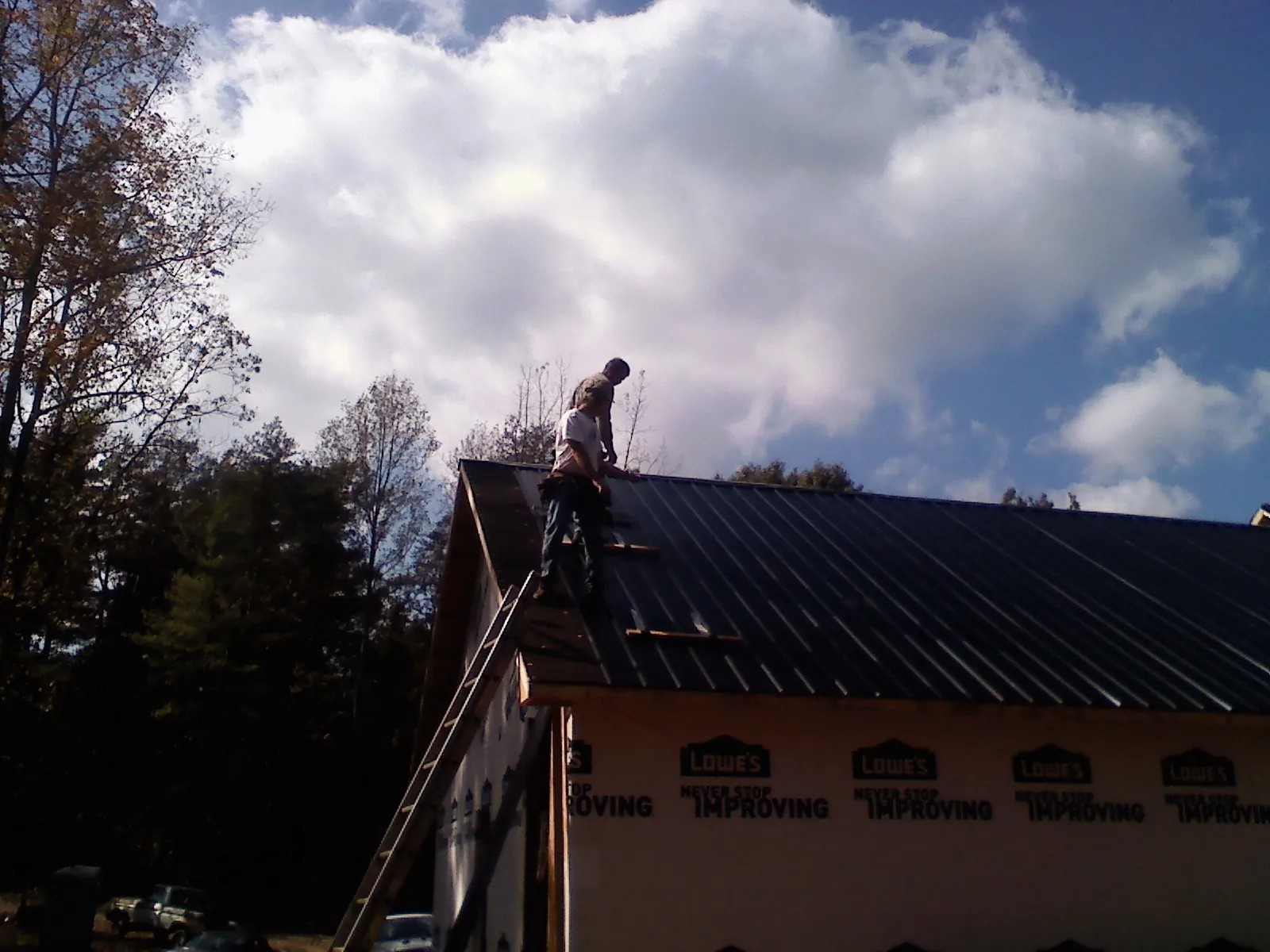 Roofer fastening dark metal panels high against a cloudy sky, from a Roof Inspection job in Abington